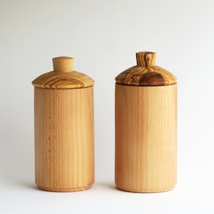 Può includere: Due contenitori di legno con coperchi. I contenitori sono in legno marrone chiaro con una venatura naturale. I coperchi sono in legno dello stesso tipo ma hanno una venatura più scura.