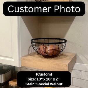May include: A custom-made wooden shelf, stained in Special Walnut, is mounted on a wall. A black wire basket holds several brown vegetables. The shelf measures 25.4 cm by 25.4 cm and is 5.08 cm thick. The text "Customer Photo" is displayed.
