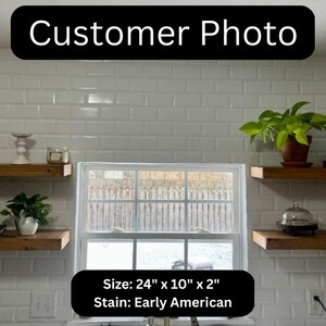 May include: A customer photo displays two wooden shelves, each measuring 61cm x 25cm x 5cm, stained in Early American. The shelves are mounted on a white tiled wall, with various decorative items.