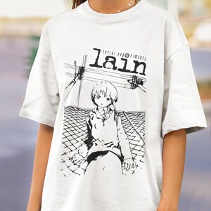 May include: White t-shirt with a black and white graphic print of a character from the anime "Serial Experiments Lain". The text "Serial Experiments Lain" is printed above the character.