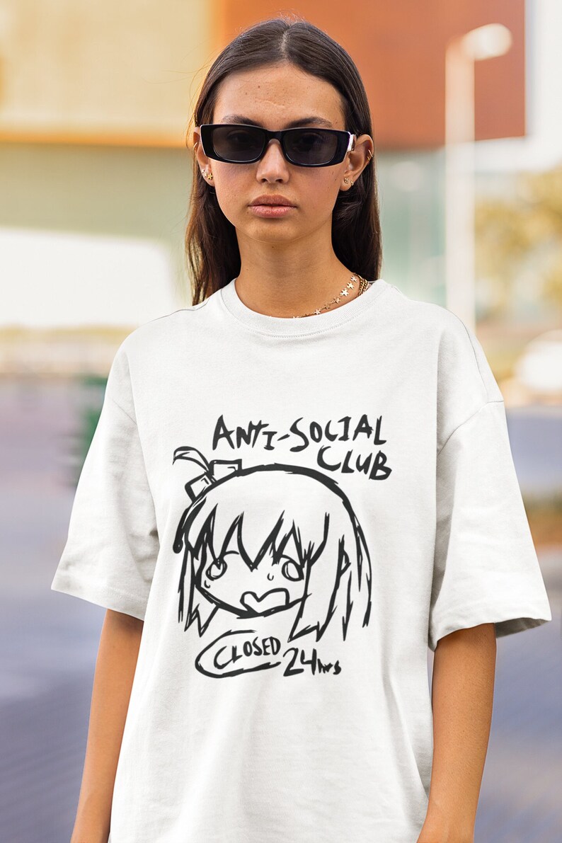 Puede incluir: Camiseta blanca con una ilustraci&oacute;n en blanco y negro de una ni&ntilde;a de dibujos animados con el texto "Anti-Social Club" y "Closed 24hrs" impreso en la parte delantera.