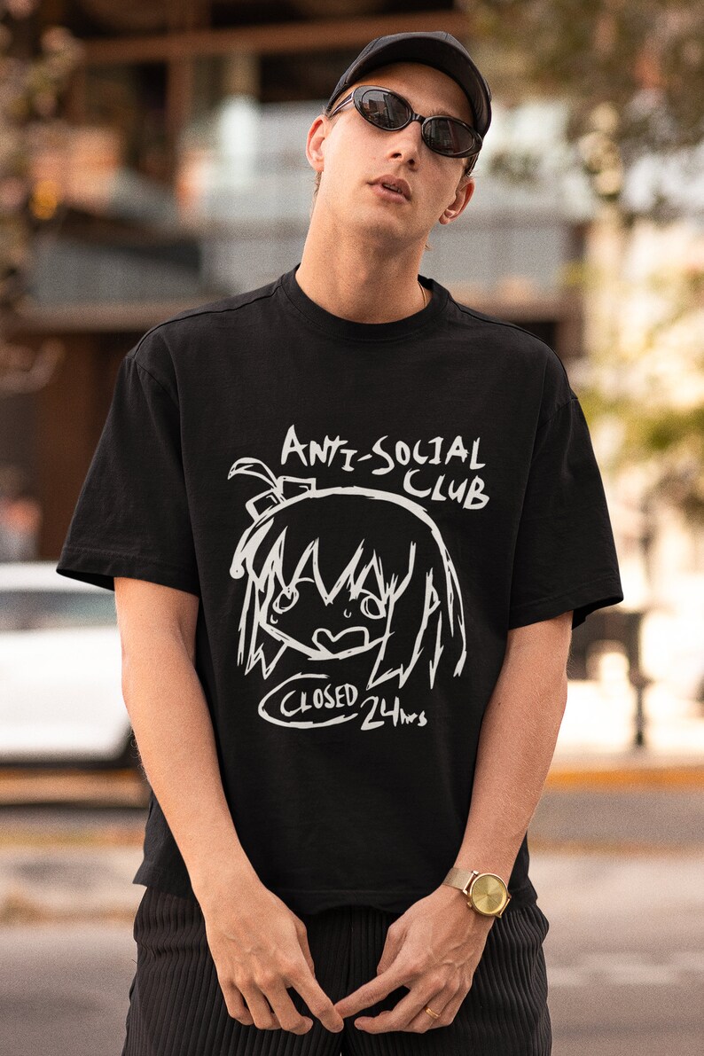 Puede incluir: Una camiseta negra con un estampado gr&aacute;fico blanco de un personaje de dibujos animados con el texto "Anti-Social Club" y "Closed 24hrs".