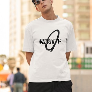 May include: White t-shirt with a black graphic design featuring a circle with a line through it and the text "結束/バド" in Japanese.