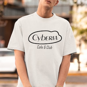 May include: A white t-shirt with a black graphic of a cloud with the text "Cyberia Cafe & Club" inside.