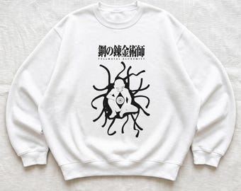 May include: A white crewneck sweatshirt featuring a black graphic print on the chest. The design displays the Japanese text 鋼の錬金術師 and the English text FULLMETAL ALCHEMIST above a stylized silhouette of a figure with an eye in its center.