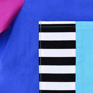 May include: A blue fabric with a pink fabric panel on the left side. A pocket is sewn on the right side of the blue fabric. The pocket is made of black and white striped fabric and a turquoise blue fabric.