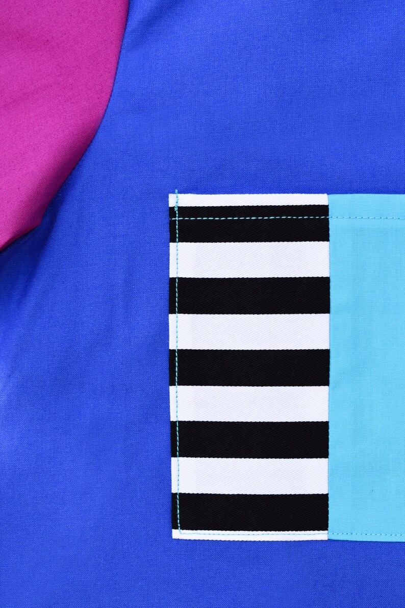 May include: A blue fabric with a pink fabric panel on the left side. A pocket is sewn on the right side of the blue fabric. The pocket is made of black and white striped fabric and a turquoise blue fabric.