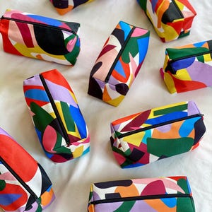 Puede incluir: Nueve estuches con cremallera de colores con patrones geom&eacute;tricos abstractos en tonos de rojo, amarillo, azul, verde, negro, blanco y morado.