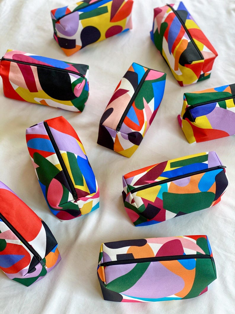 Puede incluir: Nueve estuches con cremallera de colores con patrones geom&eacute;tricos abstractos en tonos de rojo, amarillo, azul, verde, negro, blanco y morado.