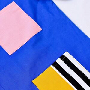 May include: A blue shirt with a pink pocket and a yellow pocket with black and white stripes. The shirt has a single button.