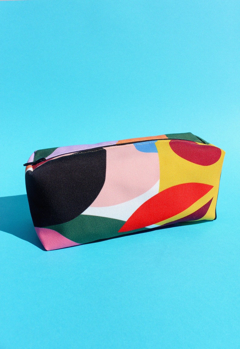 Puede incluir: Una bolsa con cremallera de patr&oacute;n geom&eacute;trico colorido con un dise&ntilde;o negro, rosa, verde, amarillo, rojo y morado.