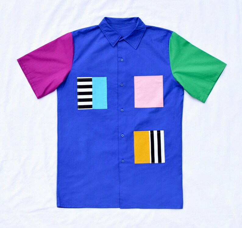 May include: A blue short-sleeved button-down shirt with a pink, green, and black and white striped patchwork design.