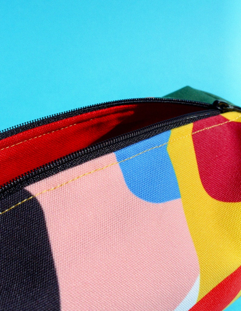 Puede incluir: Una bolsa con cremallera colorida con un patr&oacute;n geom&eacute;trico en tonos de rojo, amarillo, azul, rosa y negro. La bolsa est&aacute; abierta, revelando un forro rojo.