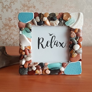 Può includere: Cornice per foto bianca decorata con pietre colorate e vetro di mare. La cornice ha un passepartout bianco e la parola "Relax" scritta in corsivo nero.