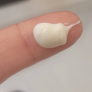 May include: A close-up of a white, creamy lotion on a fingertip.