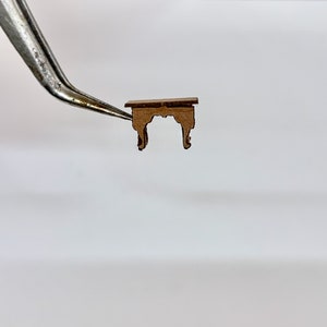 以下が含まれることがあります： シンプルなデザインの小さな茶色の木製テーブル。テーブルは長方形の天板と、装飾的なディテールが施された4本の脚を持っています。