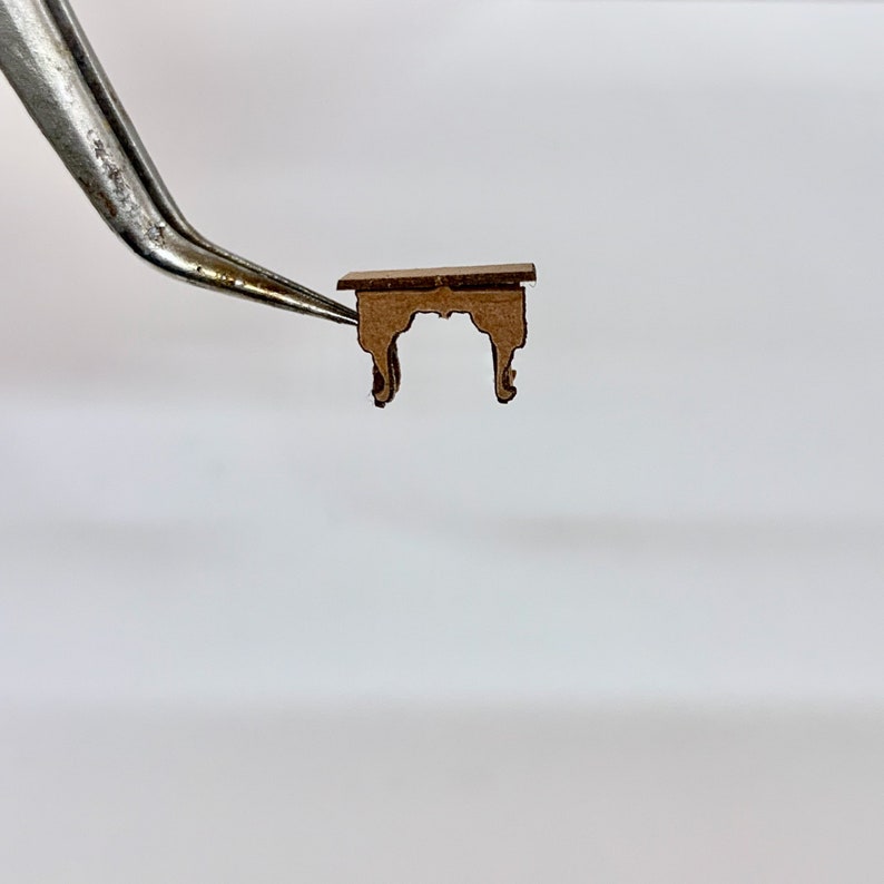 以下が含まれることがあります： シンプルなデザインの小さな茶色の木製テーブル。テーブルは長方形の天板と、装飾的なディテールが施された4本の脚を持っています。