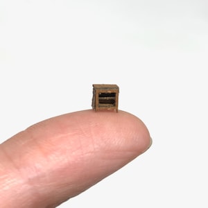 May include: A miniature wooden cabinet with two shelves. The cabinet is brown and has a rustic finish. It is small enough to fit on a fingertip.