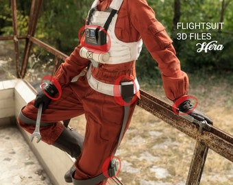 May include: A red flight suit with a white chest piece and black accents. The suit has a variety of pouches and straps. The suit is worn by a person standing on a rusty metal railing. The text "FLIGHTSUIT 3D FILES Hera" is visible in the upper right corner of the image.