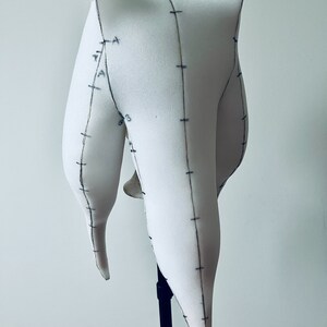 K&ouml;nnte beinhalten: Wei&szlig;er Schaumstoff-Mannequin-Kopf mit Markierungen, montiert auf einem schwarzen Stativ. Der Kopf ist in Form eines langen, spitzen Ovals mit abgerundeter Oberseite.