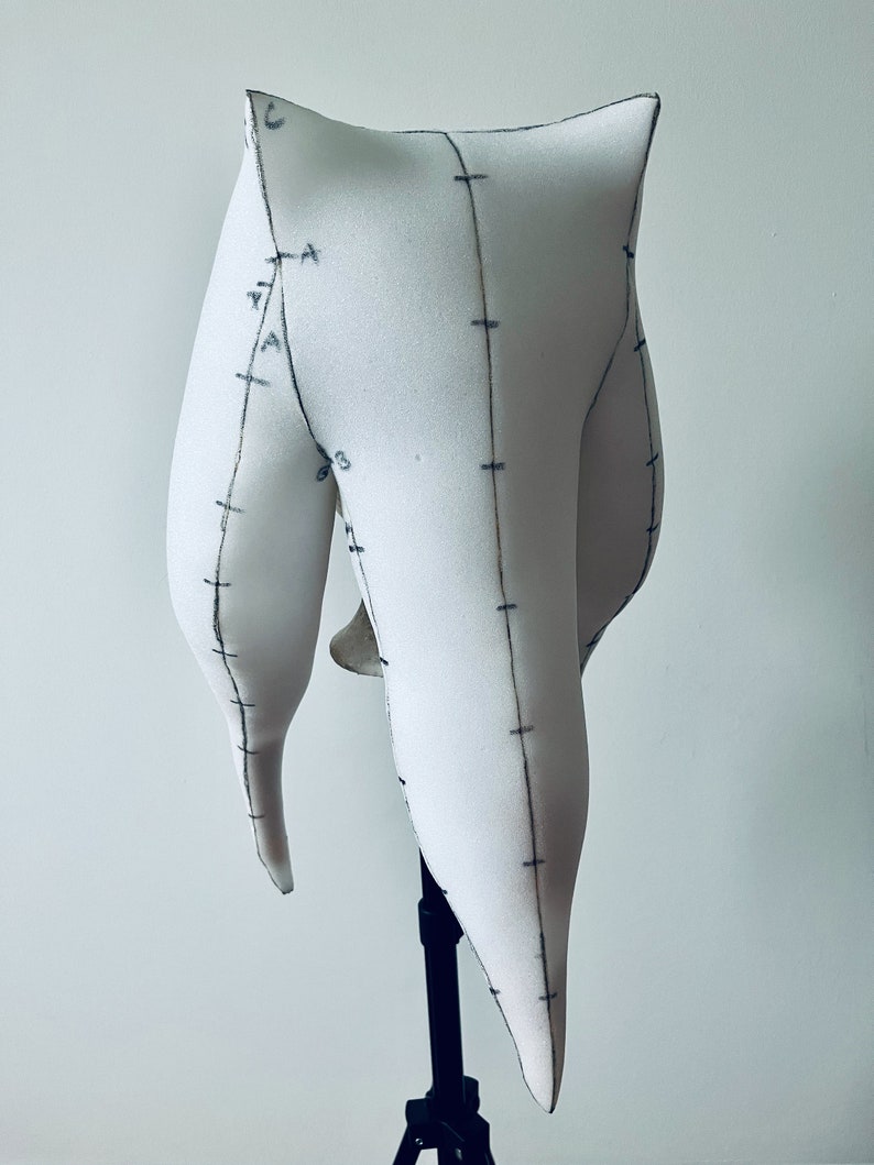 K&ouml;nnte beinhalten: Wei&szlig;er Schaumstoff-Mannequin-Kopf mit Markierungen, montiert auf einem schwarzen Stativ. Der Kopf ist in Form eines langen, spitzen Ovals mit abgerundeter Oberseite.
