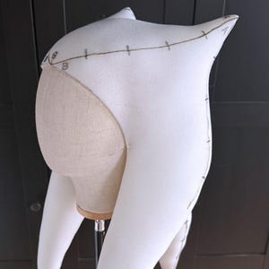 May include: A white foam headpiece with pointed ears and long, curved extensions. The headpiece is on a mannequin head. Brown lines and numbers are drawn on the foam, indicating measurements and design details. The background is a dark wood.