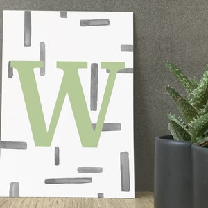 Könnte beinhalten: Weißer Kunstdruck mit einem großen, hellgrünen Buchstaben "W" und einem Muster aus grauen rechteckigen Formen. Eine Sukkulentenpflanze in einem schwarzen Topf ist rechts im Bild zu sehen.