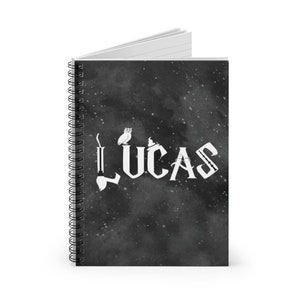 May include: A black spiral notebook with a white galaxy design and the name "LUCAS" written in a stylized font. The name is surrounded by small white images of an owl and a wizard's hat.