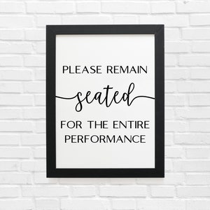 May include: Black and white sign in a black frame that reads "Please remain seated for the entire performance."