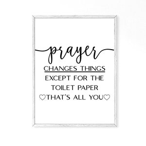 May include: A white framed print with black text that reads "prayer changes things except for the toilet paper that's all you" with two small hearts on either side of the text.