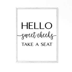 May include: A white framed print with black text that reads "HELLO sweet cheeks TAKE A SEAT".