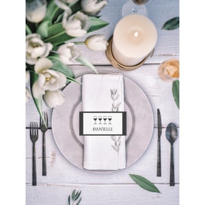 May include: A white place card with a black border and a simple design of four wine glasses and the name "Danielle" printed in black.