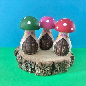May include: Three mushroom-shaped houses with painted doors and colourful flags. The houses are on a wooden slice.