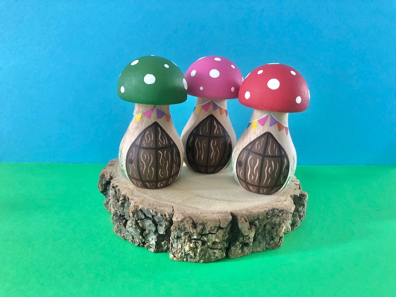 May include: Three mushroom-shaped houses with painted doors and colourful flags. The houses are on a wooden slice.