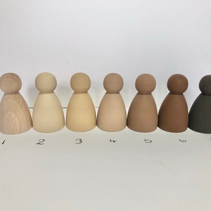 May include: Seven wooden figures in a row, painted in shades of brown, from light to dark. The figures are all the same size and shape, with a rounded head and a bell-shaped body.
