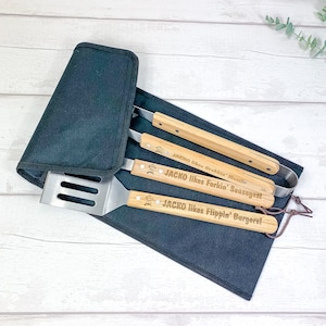 May include: A set of three grilling tools with wooden handles and stainless steel heads. The handles are engraved with the text "JACKO likes Gribblin' Meat", "JACKO likes Forkin' Sausages", and "JACKO likes Flippin' Burgers!" The tools are in a black canvas carrying case.