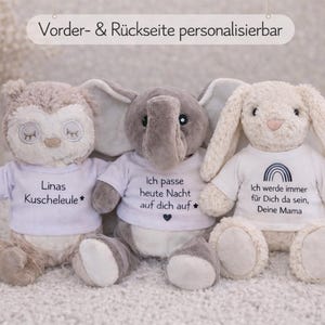 Könnte beinhalten: Drei Stofftiere: eine Eule, ein Elefant und ein Hase, jeweils mit einem weißen T-Shirt mit Text. Die Eule ist hellbraun, der Elefant grau und der Hase cremefarben. Der Text auf den Shirts ist personalisierbar.
