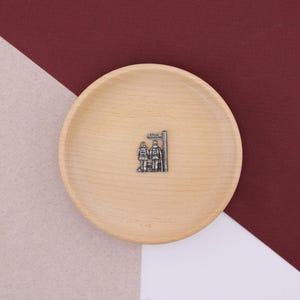 Könnte beinhalten: Eine Holzschale mit einem silbernen Anhänger, der zwei Figuren zeigt, die an einem Wegweiser stehen.