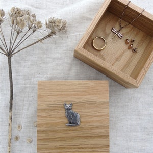 May include: A wooden box with a cat design on the lid. The box is open and shows a dragonfly necklace, a ring, and earrings inside.