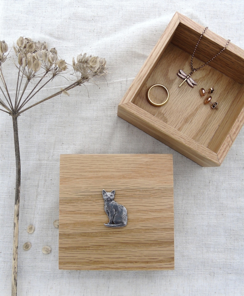 May include: A wooden box with a cat design on the lid. The box is open and shows a dragonfly necklace, a ring, and earrings inside.