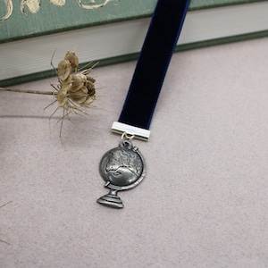 May include: A blue velvet bookmark with a silver globe charm. The globe is detailed with continents and oceans.