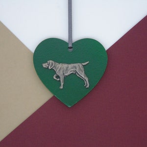 May include: A green heart-shaped ornament with a silver-colored dog silhouette. The ornament is hanging from a gray ribbon.