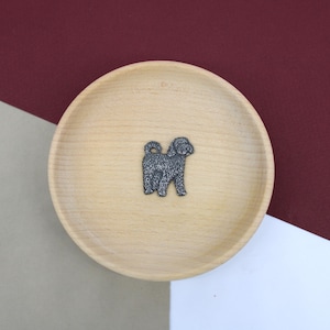 May include: A small, black, furry dog figurine on a wooden plate. The dog is standing on all four legs and has its tail curled up.