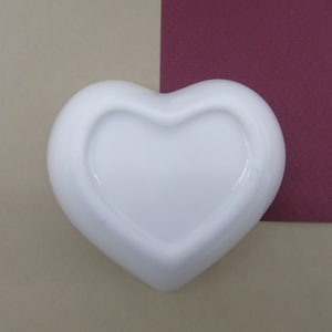 May include: A white ceramic heart-shaped dish with a smooth, glossy finish. The dish is empty and ready to be filled with treats or trinkets.
