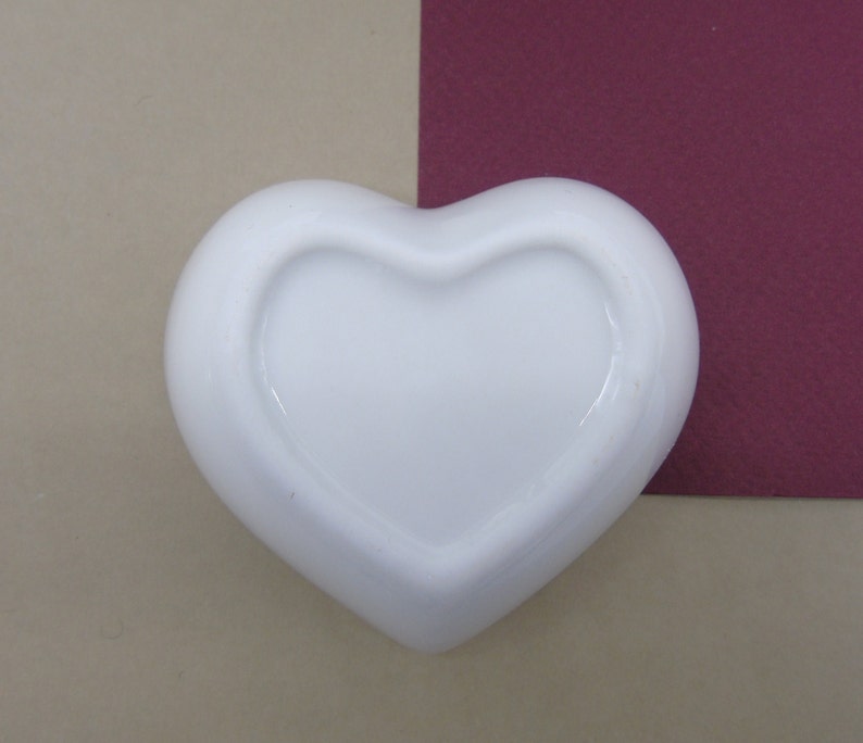 May include: A white ceramic heart-shaped dish with a smooth, glossy finish. The dish is empty and ready to be filled with treats or trinkets.