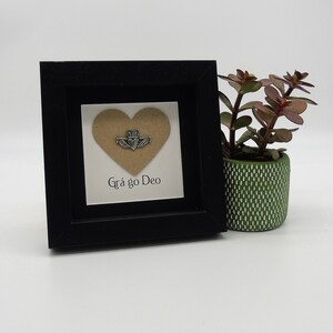 May include: A small black framed picture with a brown heart cutout and a silver Celtic knot design. The text "Gr&aacute; go Deo" is written below the heart.