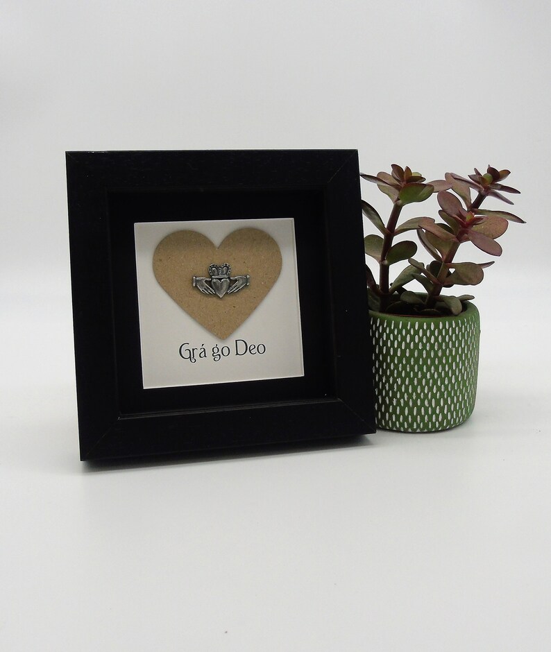May include: A small black framed picture with a brown heart cutout and a silver Celtic knot design. The text "Gr&aacute; go Deo" is written below the heart.