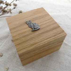 May include: A wooden box with a cat figurine on the lid. The box is made of light brown wood with a natural grain pattern.