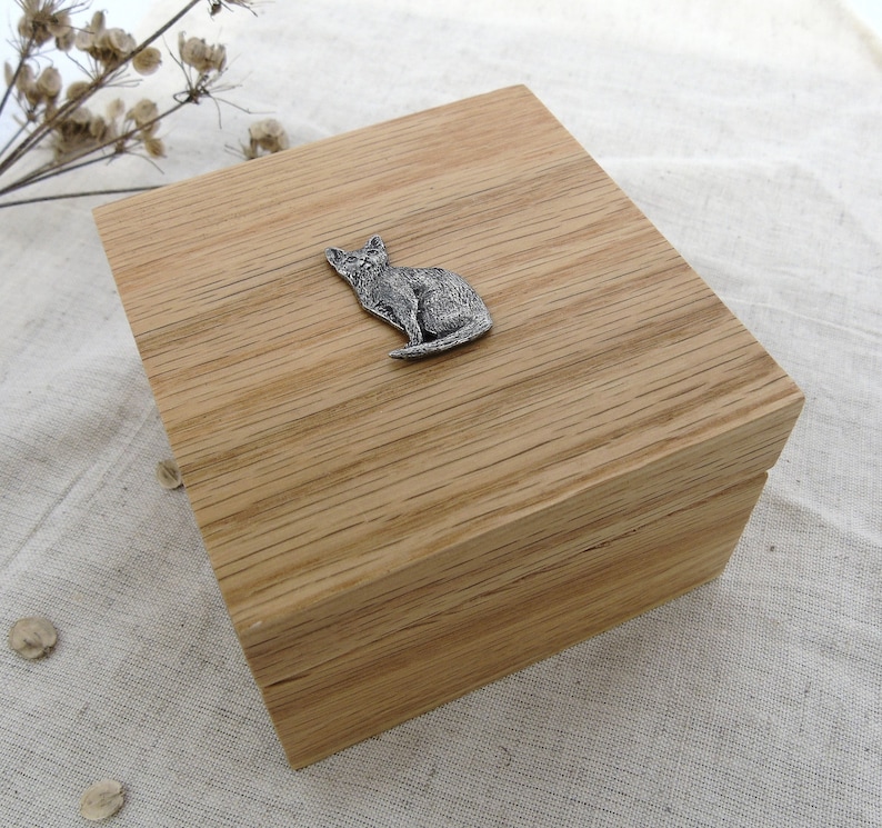 May include: A wooden box with a cat figurine on the lid. The box is made of light brown wood with a natural grain pattern.