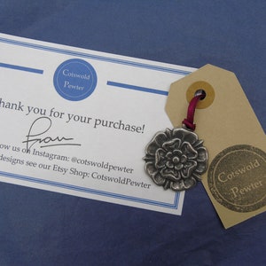 May include: A thank you card from Cotswold Pewter with a silver charm of a white rose on a brown tag. The card says "Thank you for your purchase!" and includes contact information for the shop on Instagram and Etsy.